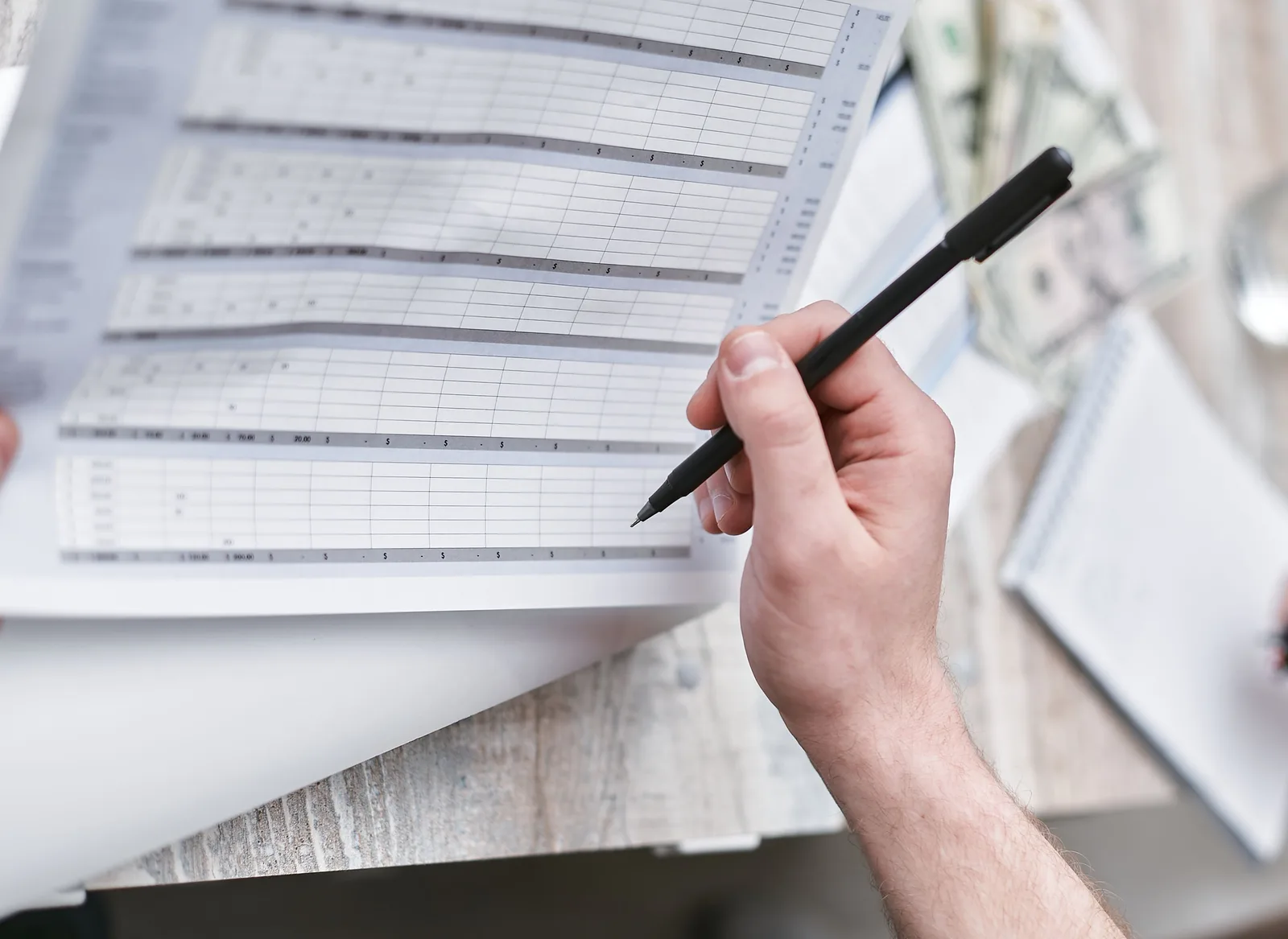 A close-up of a person holding a pen reviewing a financial document with cash visible, ideal for business themes. How to build ecommerce advertising benchmarks from your own data