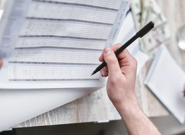 A close-up of a person holding a pen reviewing a financial document with cash visible, ideal for business themes. How to build ecommerce advertising benchmarks from your own data