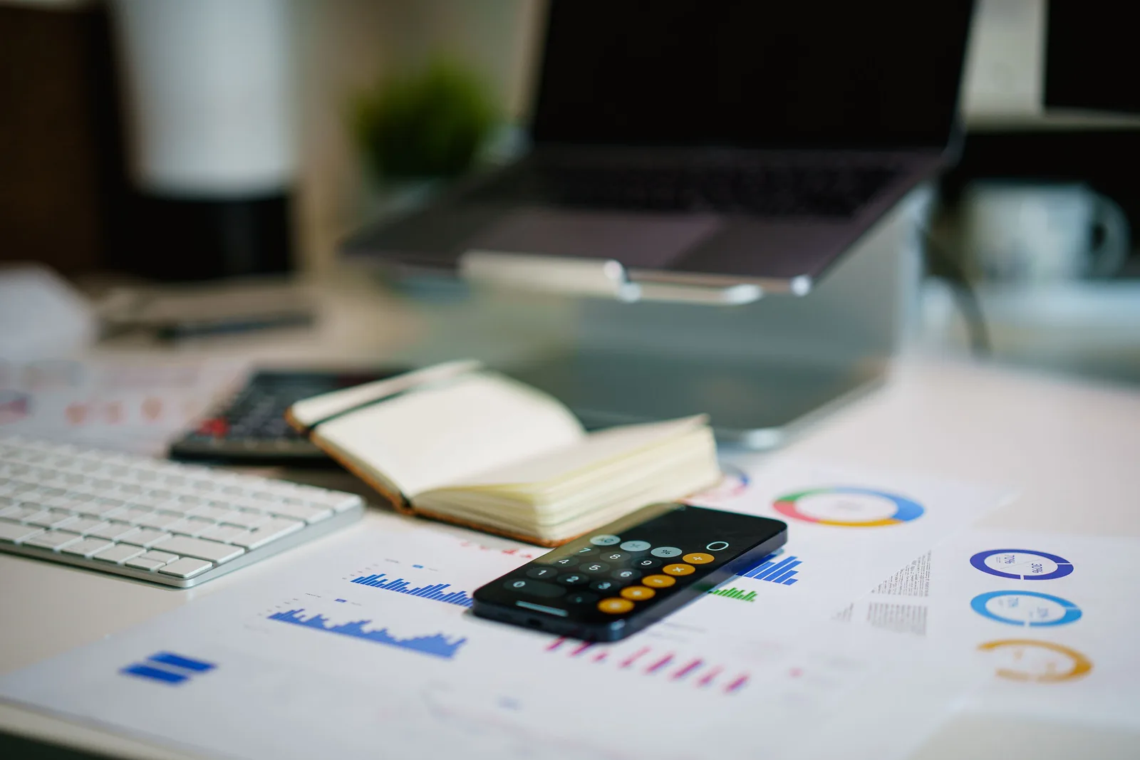 Modern office desk with a laptop, smartphone calculator app, and financial charts. Reading ecommerce marketing strategy benchmarks in context