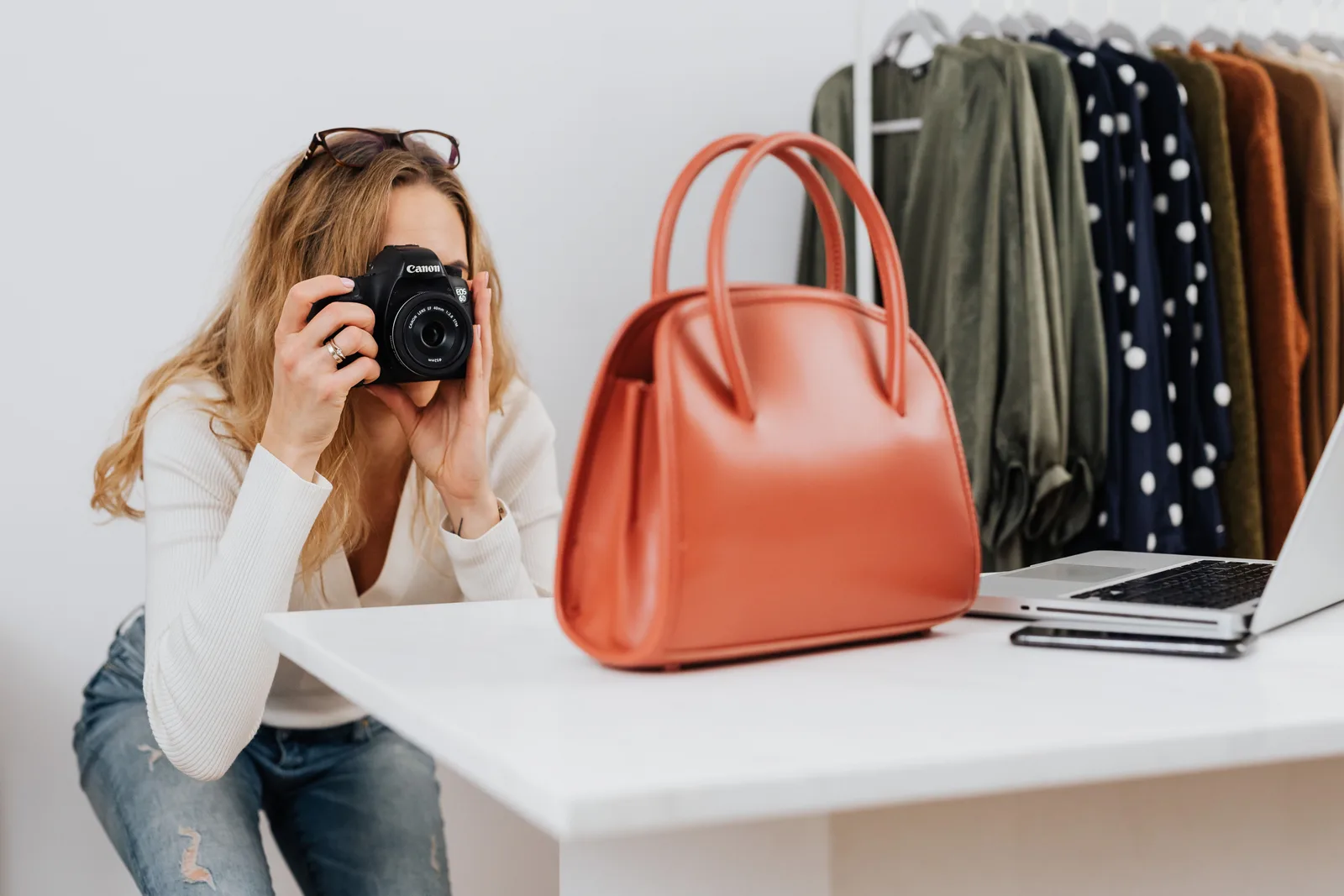 Caucasian woman capturing handbag photos for online fashion retail with camera. The ecommerce marketing strategy best practices worth adopting first
