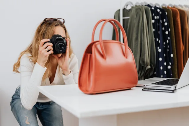 Caucasian woman capturing handbag photos for online fashion retail with camera. The ecommerce marketing strategy best practices worth adopting first