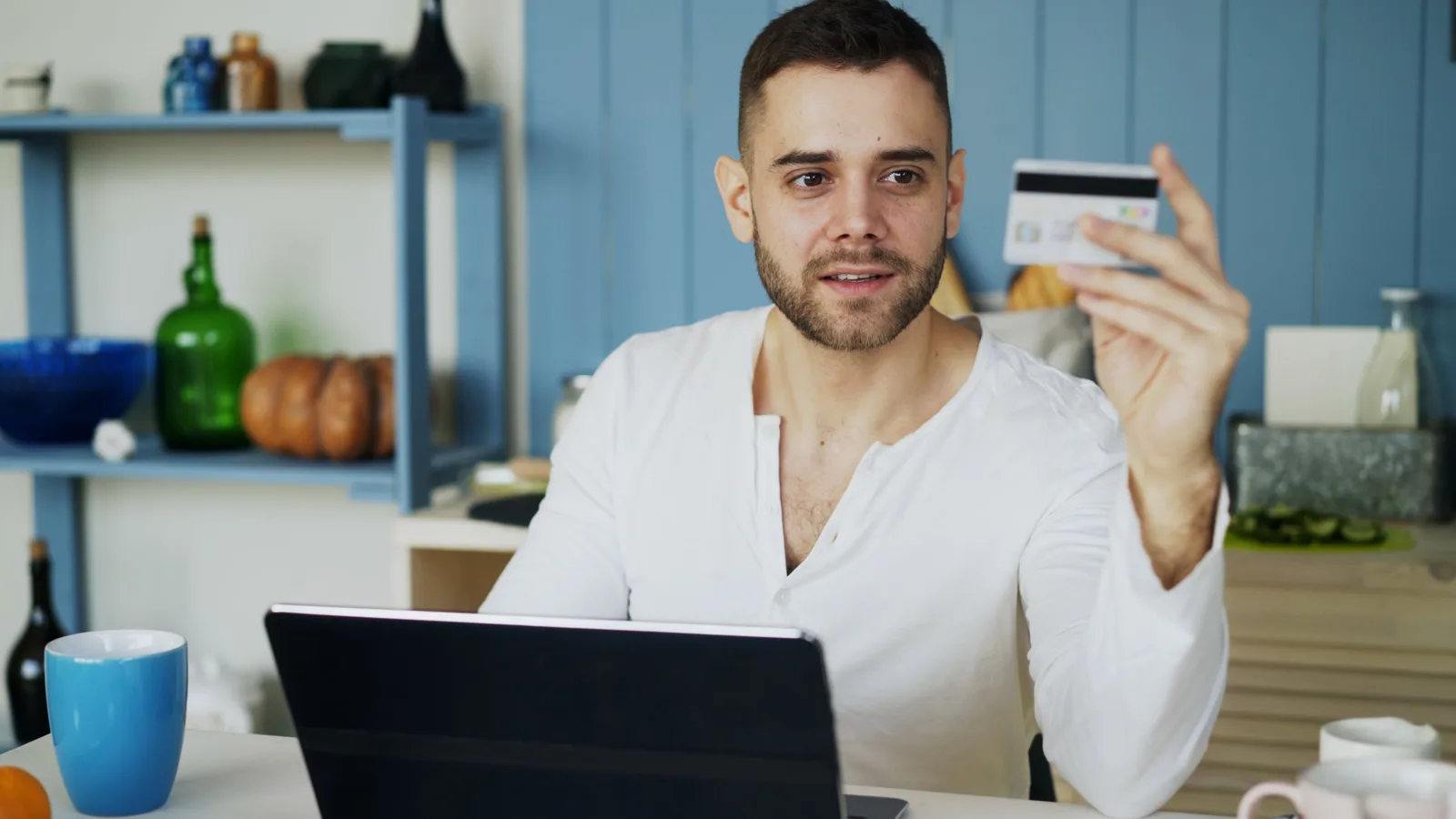 A man in a white shirt sits at a desk, using a laptop and holding a credit card. Ecommerce SEO examples: five named stores and platforms